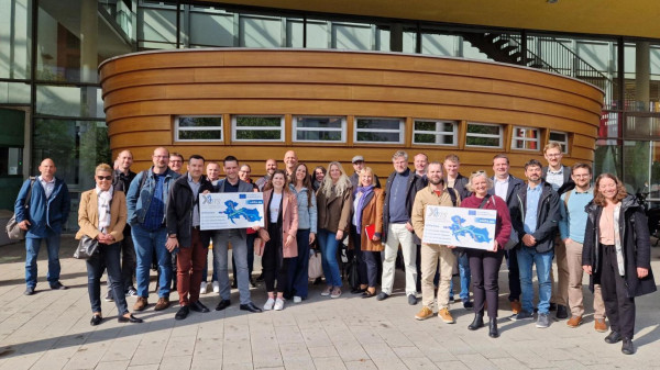 Gruppe der X4ITS Teilnehmenden stehen vor einem Gebäude und halten Schilder mit den teilnehmenden Ländern in die Luft.