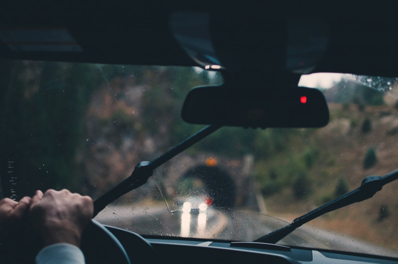 Rear-view-car-mirror in a car and somebody's hands on a steering wheel, outside it's raining